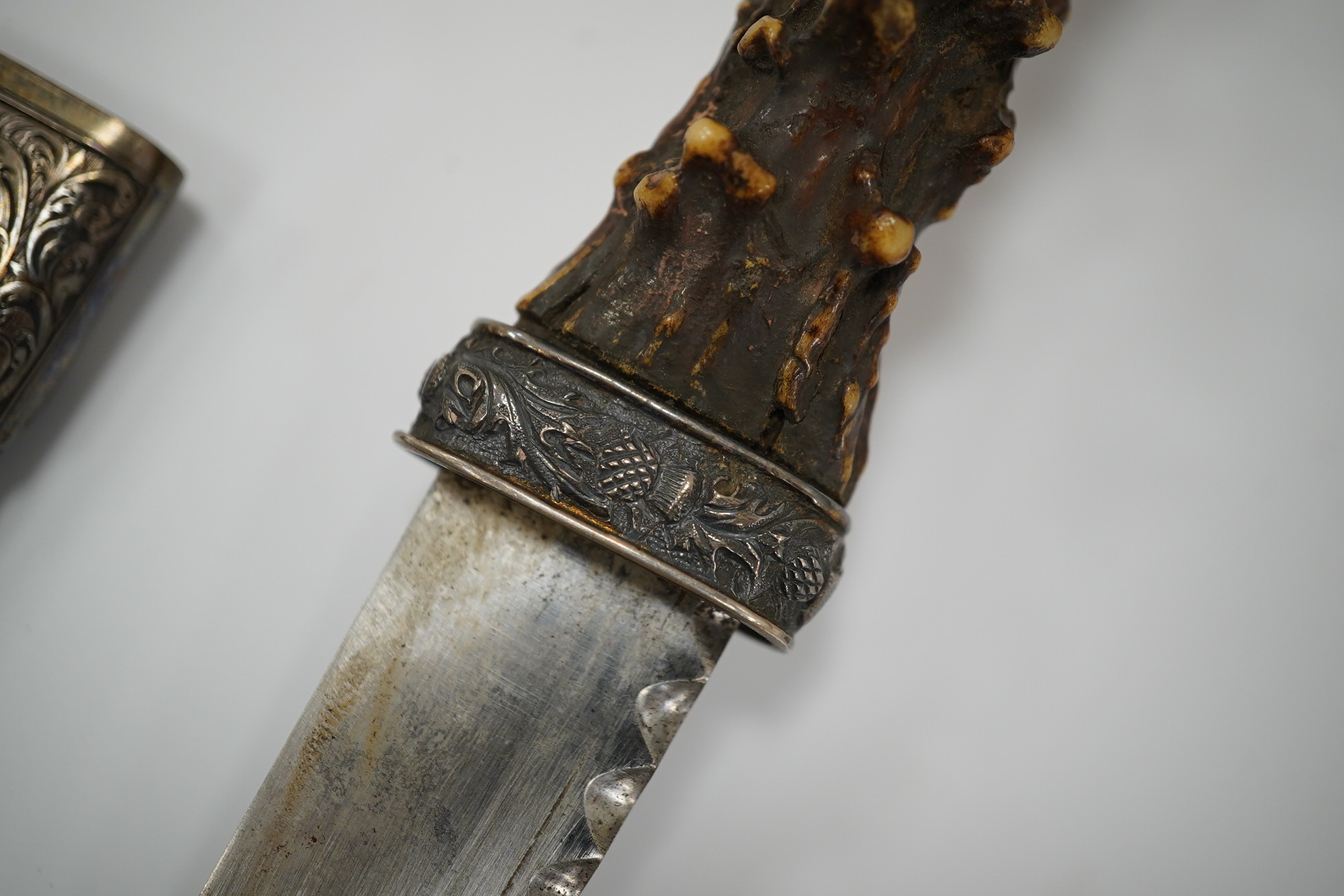 A late 19th century Scottish traditional sgian dubh with foiled glass mounted deer antler handle, and silver coloured metal mounts with thistles in relief, blade 10cm. Condition - fair, missing chape.